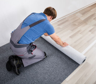 72565577 - young male handyman rolling carpet on floor at home